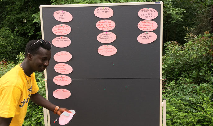 Ein Teilnehmer pinnt runde Moderationskarten an eine Pinnwand im Garten der Berckstrasse