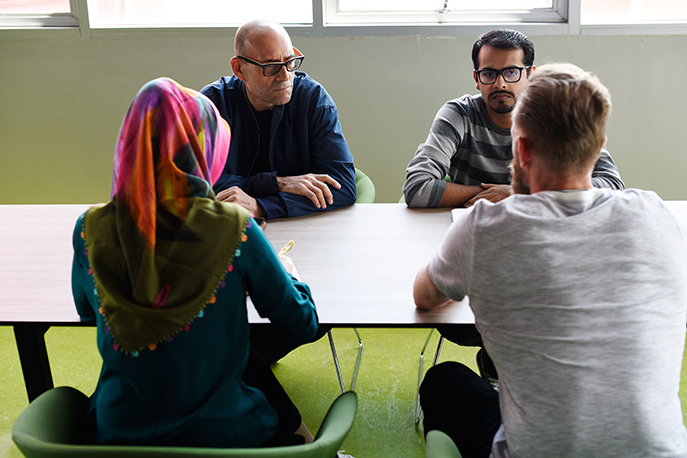 Um einen Tisch sitzen junge Geflüchtete mit Menschen, die beim Deutsch lernen helfen