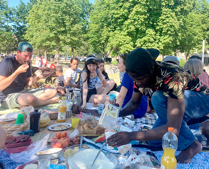 Diverse junge Menschen sitzen im Sommer auf bunten Decken und Picknicken